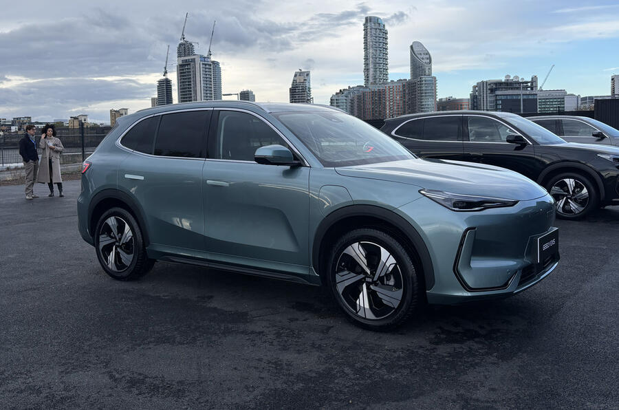 A red hatchback car parked on the street, with a person standing nearby.