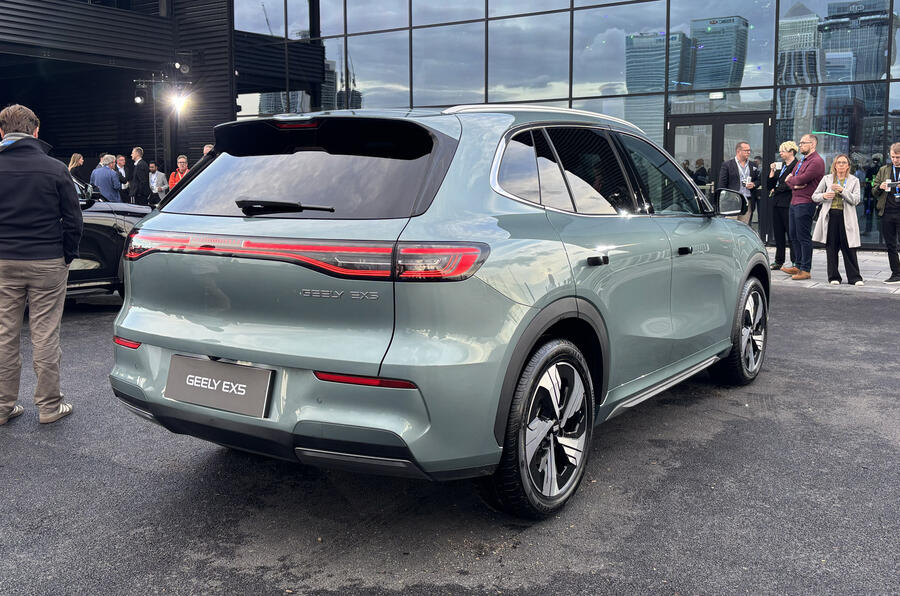 A silver hatchback car parked on the side of a city street, with a visible license plate and a person standing nearby, possibly the driver.