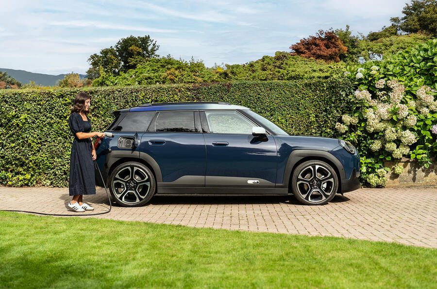 A person standing next to a parked car, showcasing its sleek design and shiny wheels, with a focus on the vehicle's modern features.